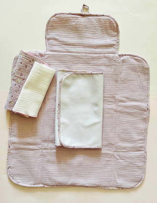 Cambiador de paseo abierto; imagen de la parte interior de muselina color malva liso; alfombra de guata impermeable y dos muselinas de color malva liso y malva con flores