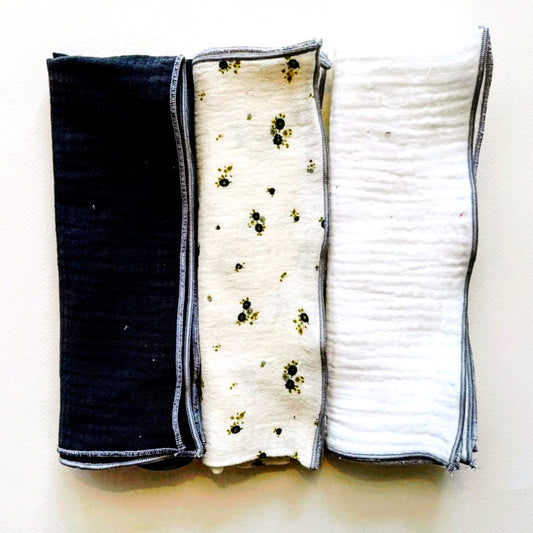 Conjunto de tres muselinas en color gris antracita la de la izquierda, beis con flores grises y verdes en el centro y blanco liso en la derecha; ambas tres con terminación de hilo gris