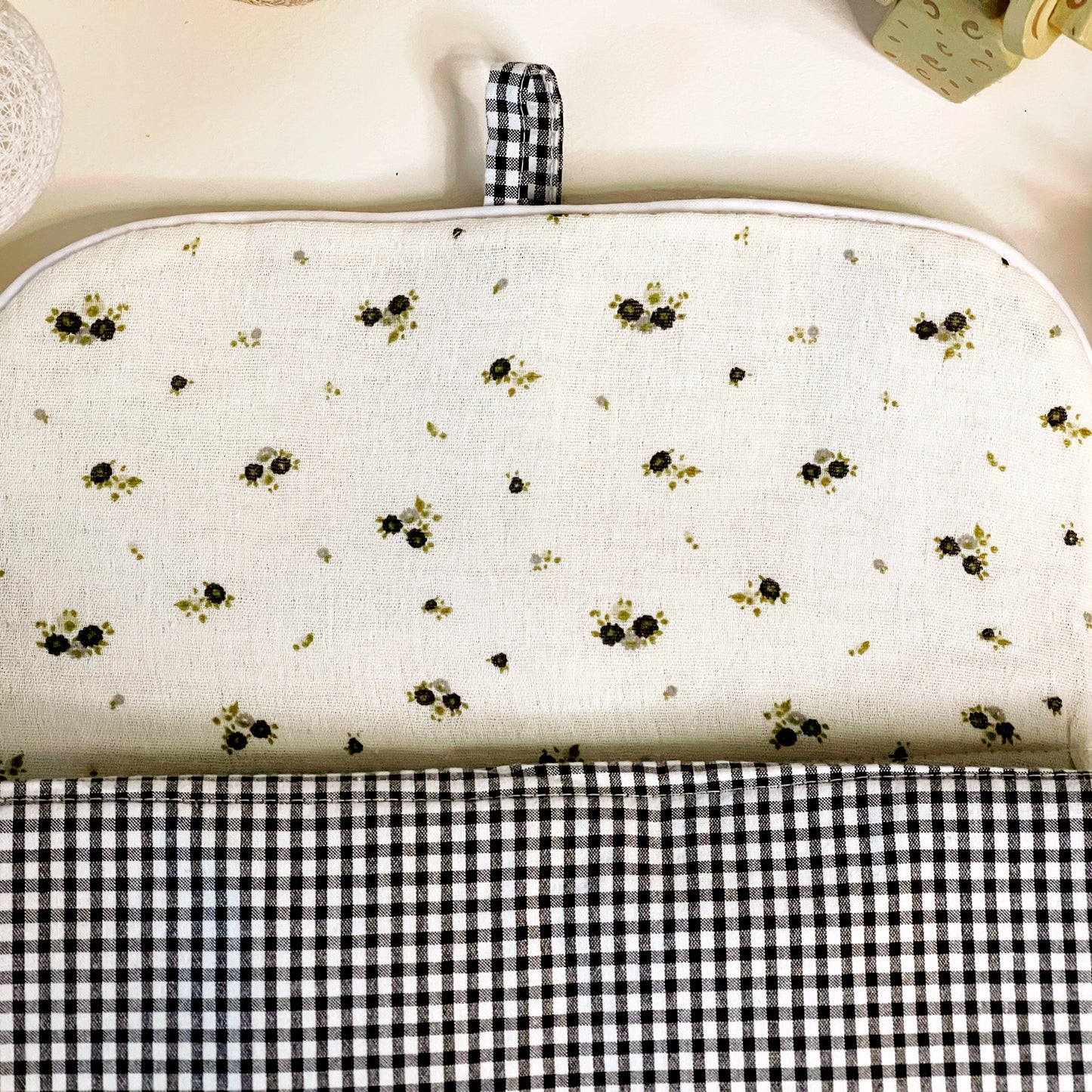 Lado interno del cambiador de paseo en muselina de color beis con flores grises y verde y en la parte exterior estampado de cuadros en color negro y blanco