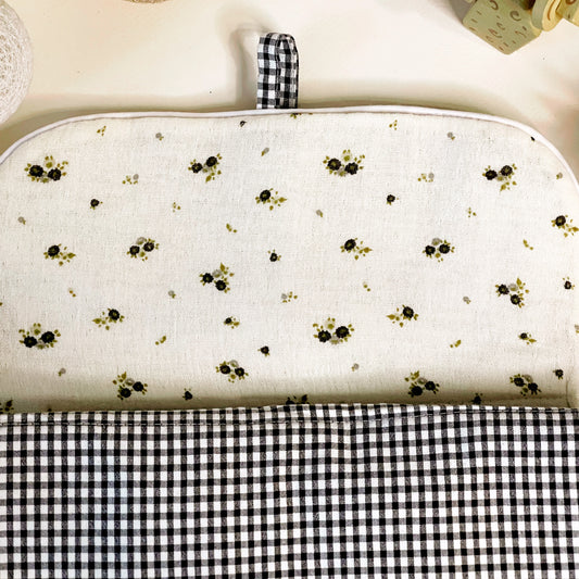 Lado interno del cambiador de paseo en muselina de color beis con flores grises y verde y en la parte exterior estampado de cuadros en color negro y blanco