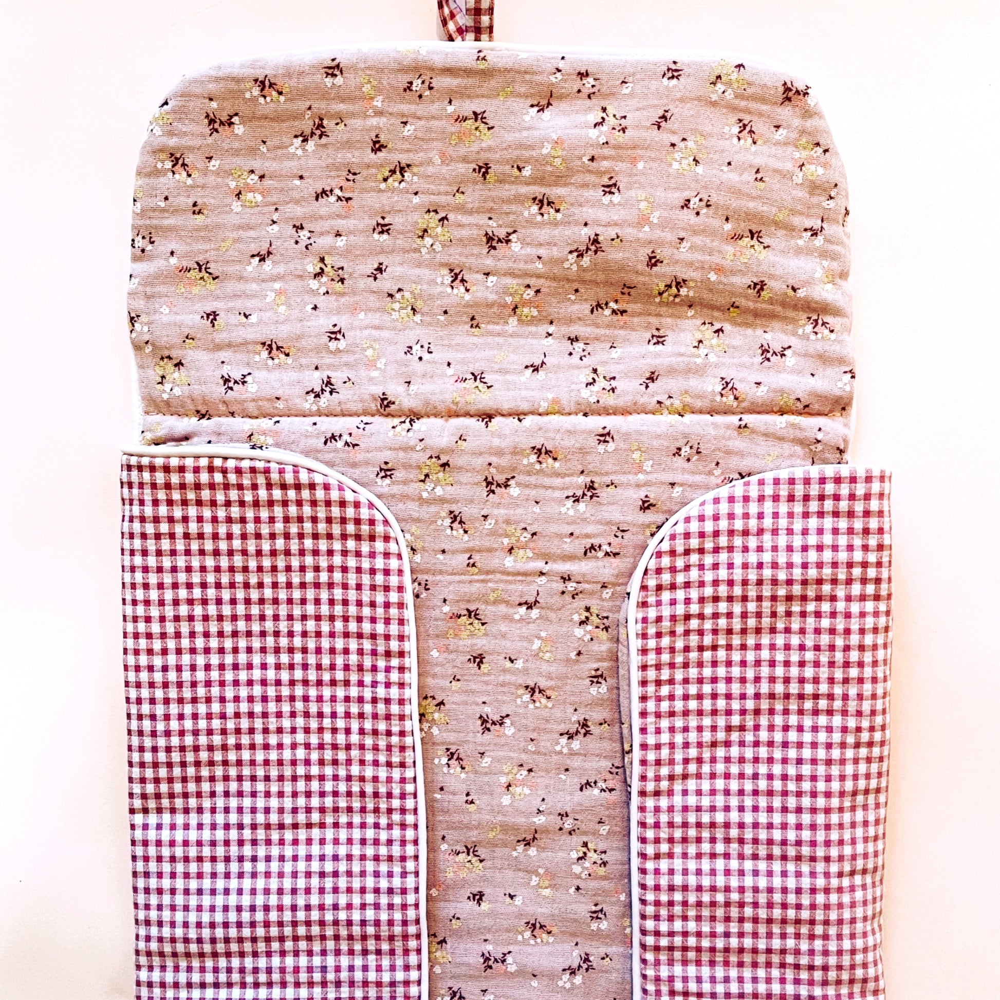 Cambiador de paseo semi abierto; en la parte exterior el tejido es de estampado de cuadros rosa y blanco y en la interior es de muselina malva de flores.