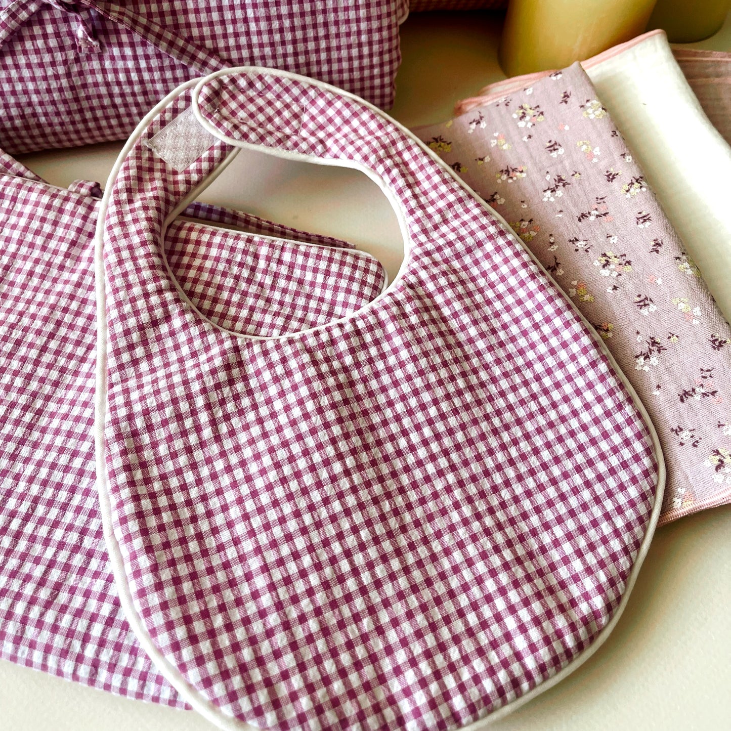 Conjunto de babero de estampado de cuadros rosas y blanco , muselinas de color malva con flores, malva liso y color blanco, porta toallitas del mismo estampado.