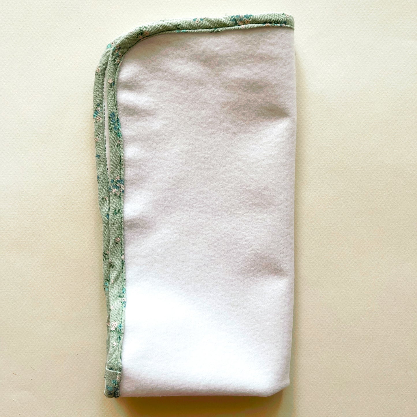  Alfombra para cambiar al bebé de color blanco y de suave guata , terminación en tejido de muselina color verde con florecitas