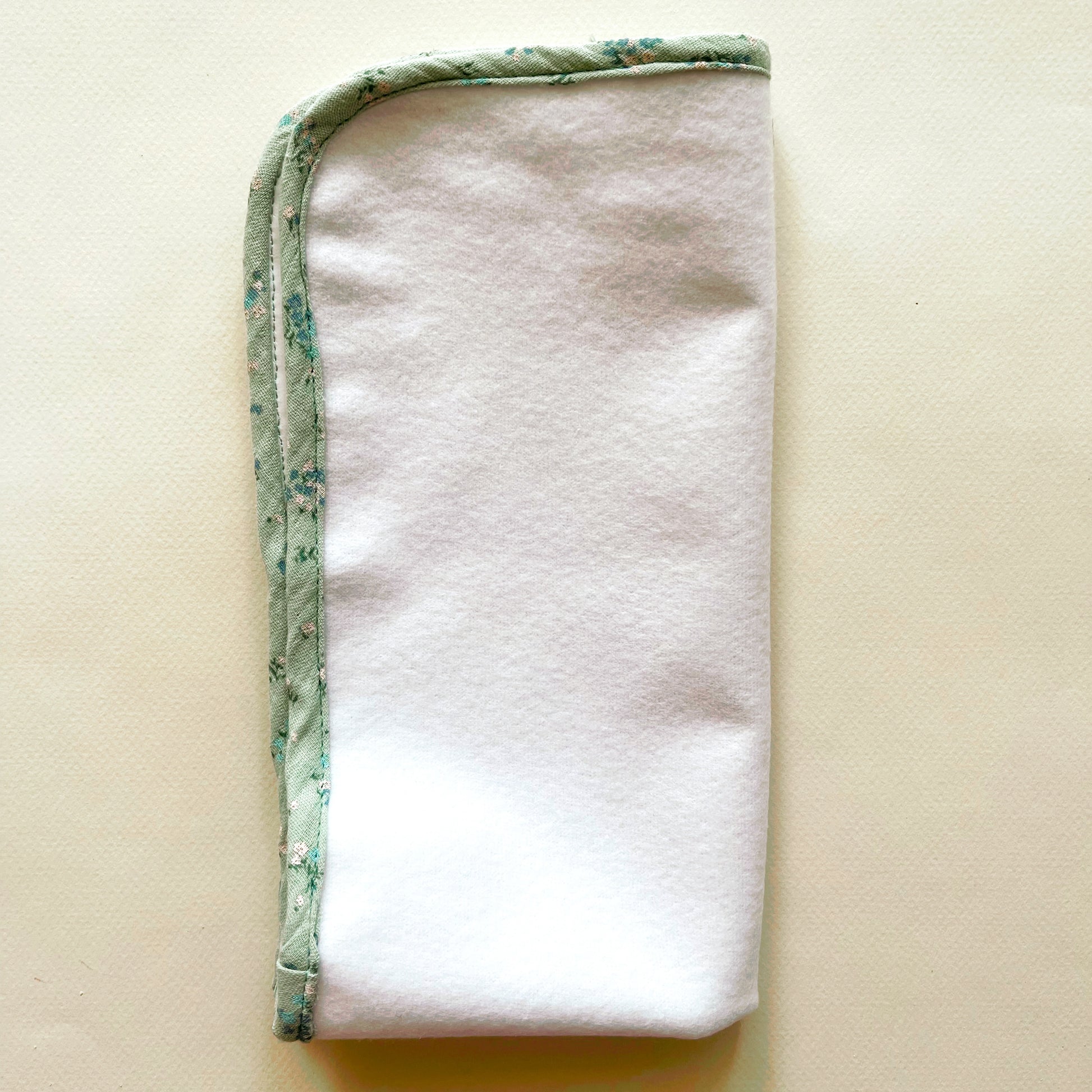  Alfombra para cambiar al bebé de color blanco y de suave guata , terminación en tejido de muselina color verde con florecitas