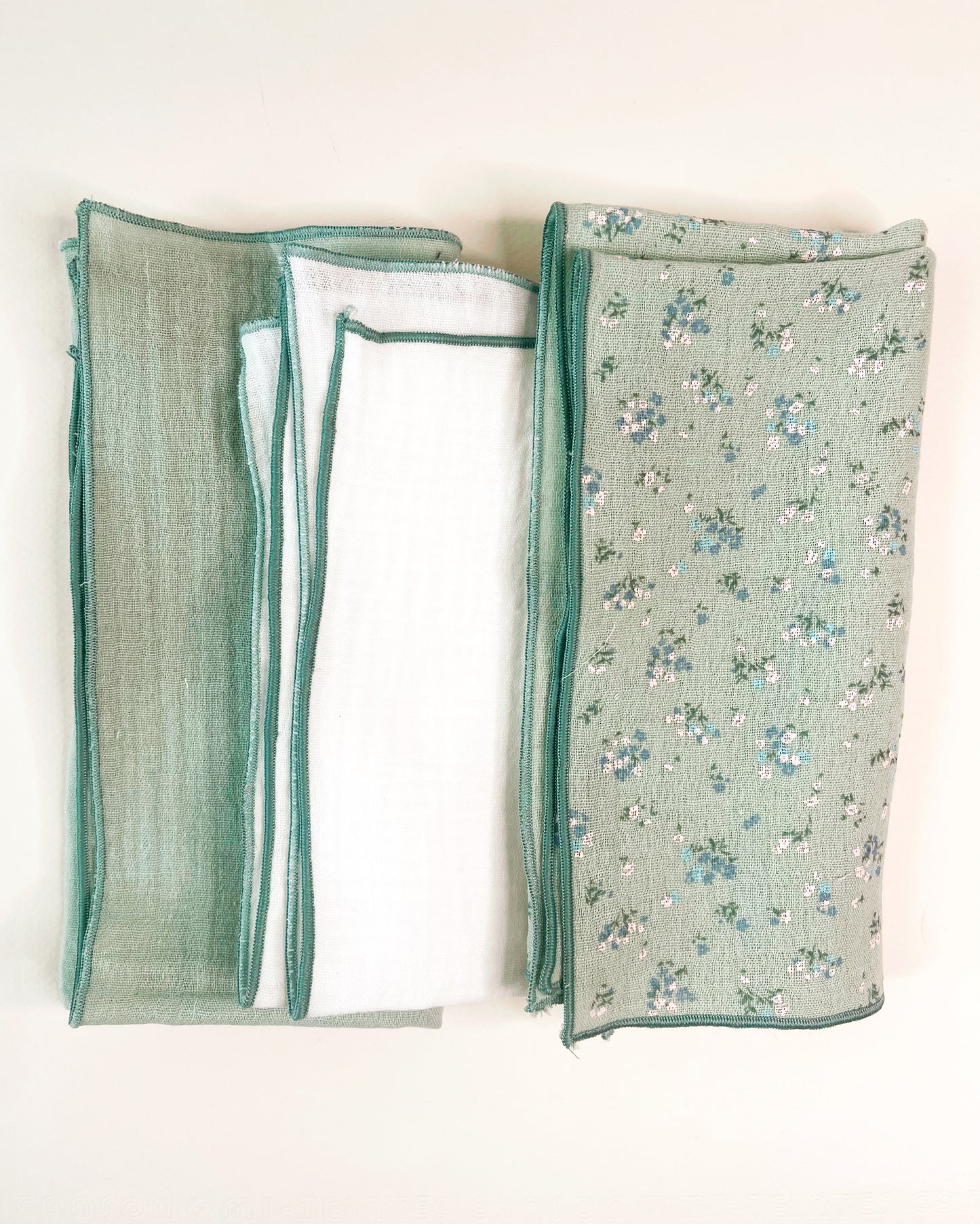 Conjunto de tres muselinas en color verde liso en la izquierda, en el centro blanco liso y a la derecha verde con florecitas azules y blancas. terminación en hilo verde