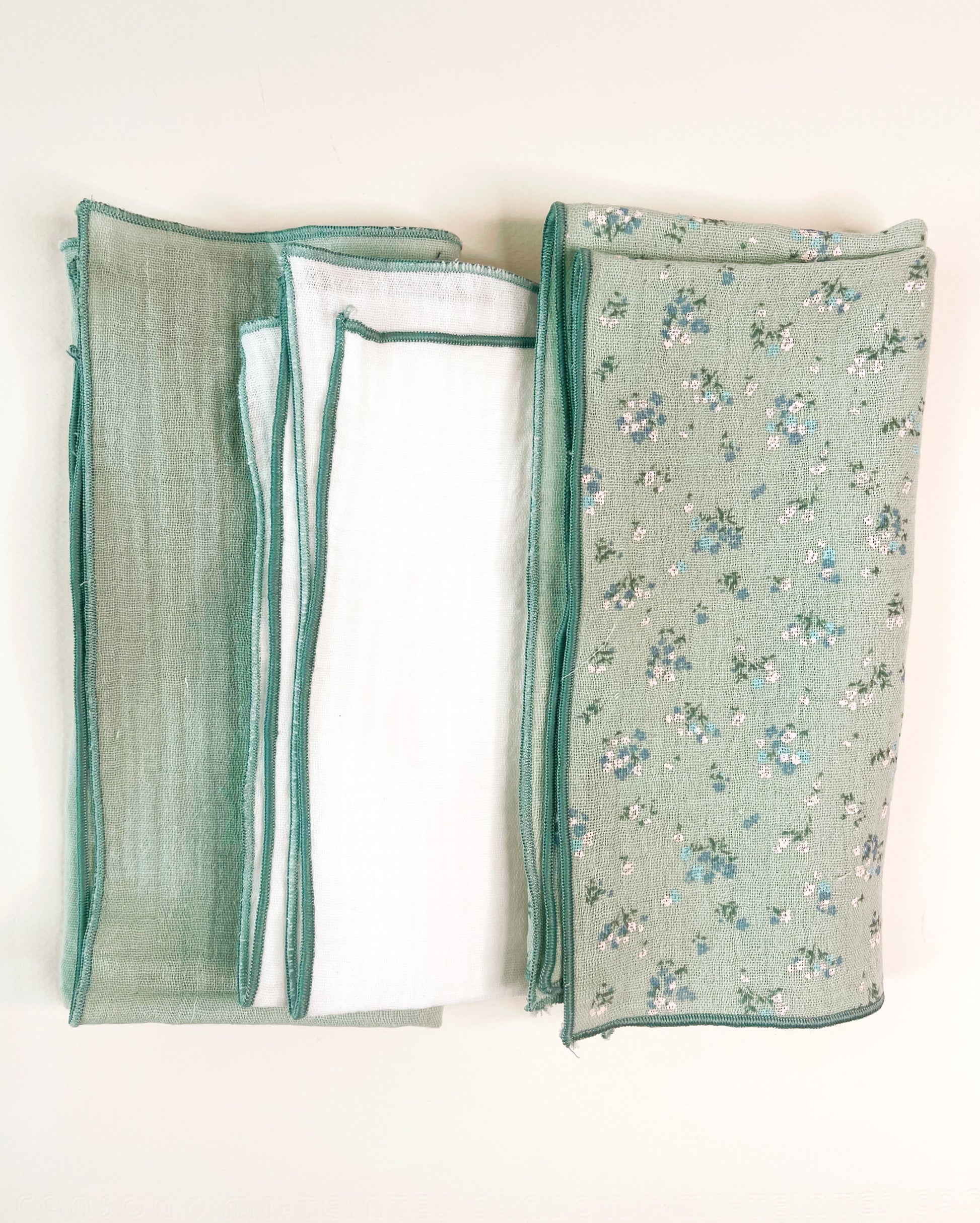 Conjunto de tres muselinas en color verde liso en la izquierda, en el centro blanco liso y a la derecha verde con florecitas azules y blancas. terminación en hilo verde