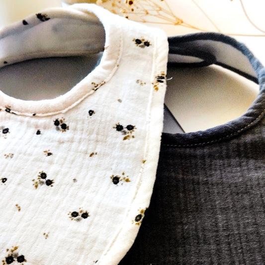 Conjunto de dos baberos en muselina de color beis con flores grises y verdes y de color gris antracita liso