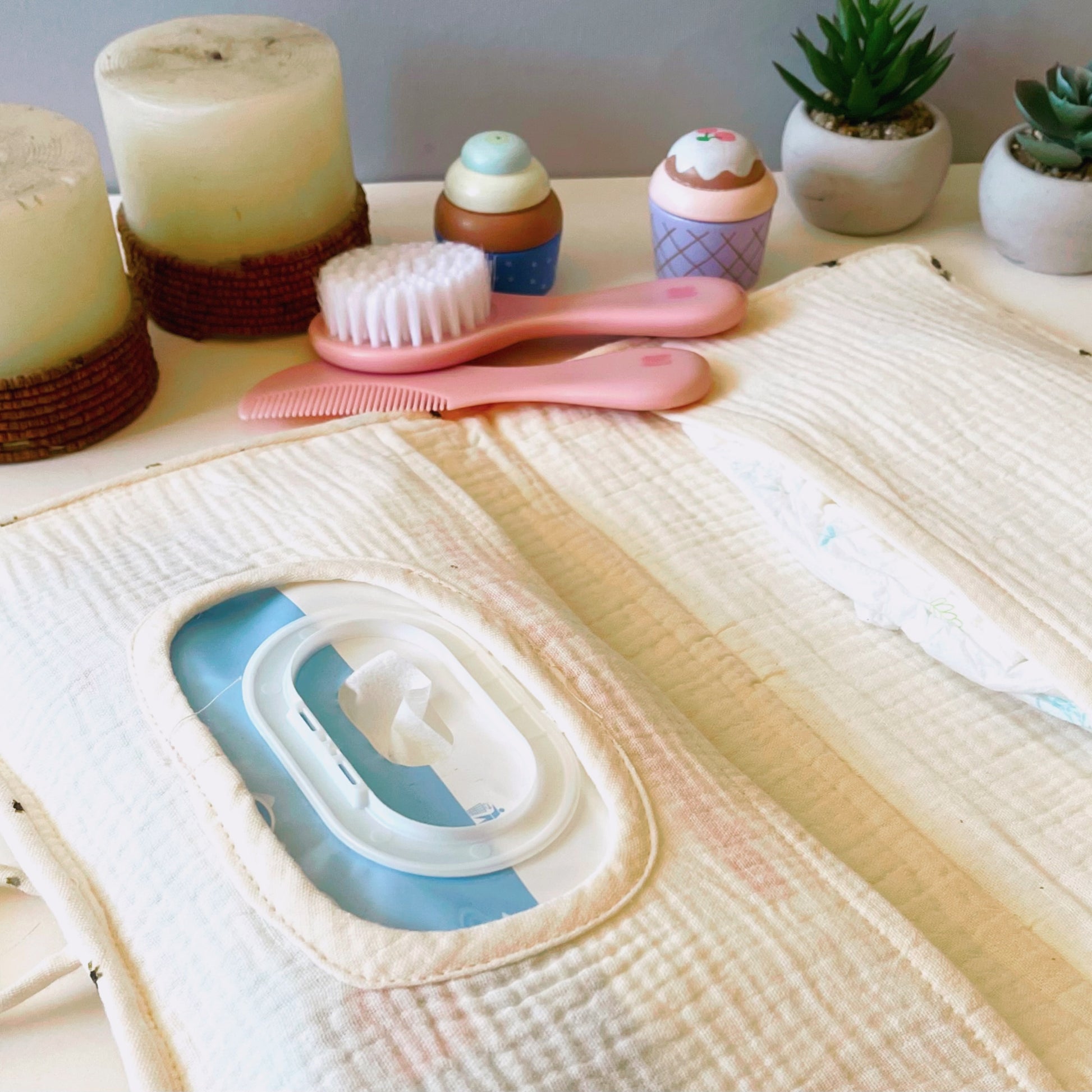 Porta toallitas abierto con tela de muselina beis liso, dos compartimentos, el de la izquierda es para meter las toallitas y el de la derecha los pañales del bebé. Decoración peine de bebé y velas