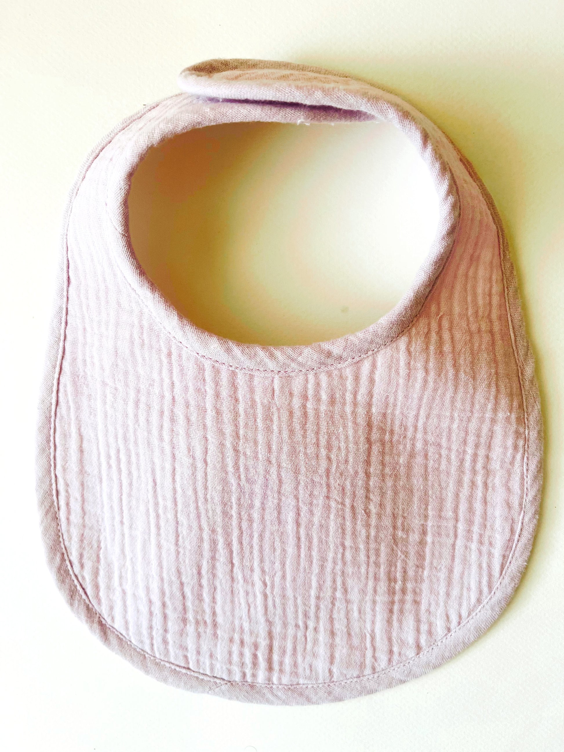 Babero de muselina color malva liso con cierre en velcro adaptable al crecimiento del bebé