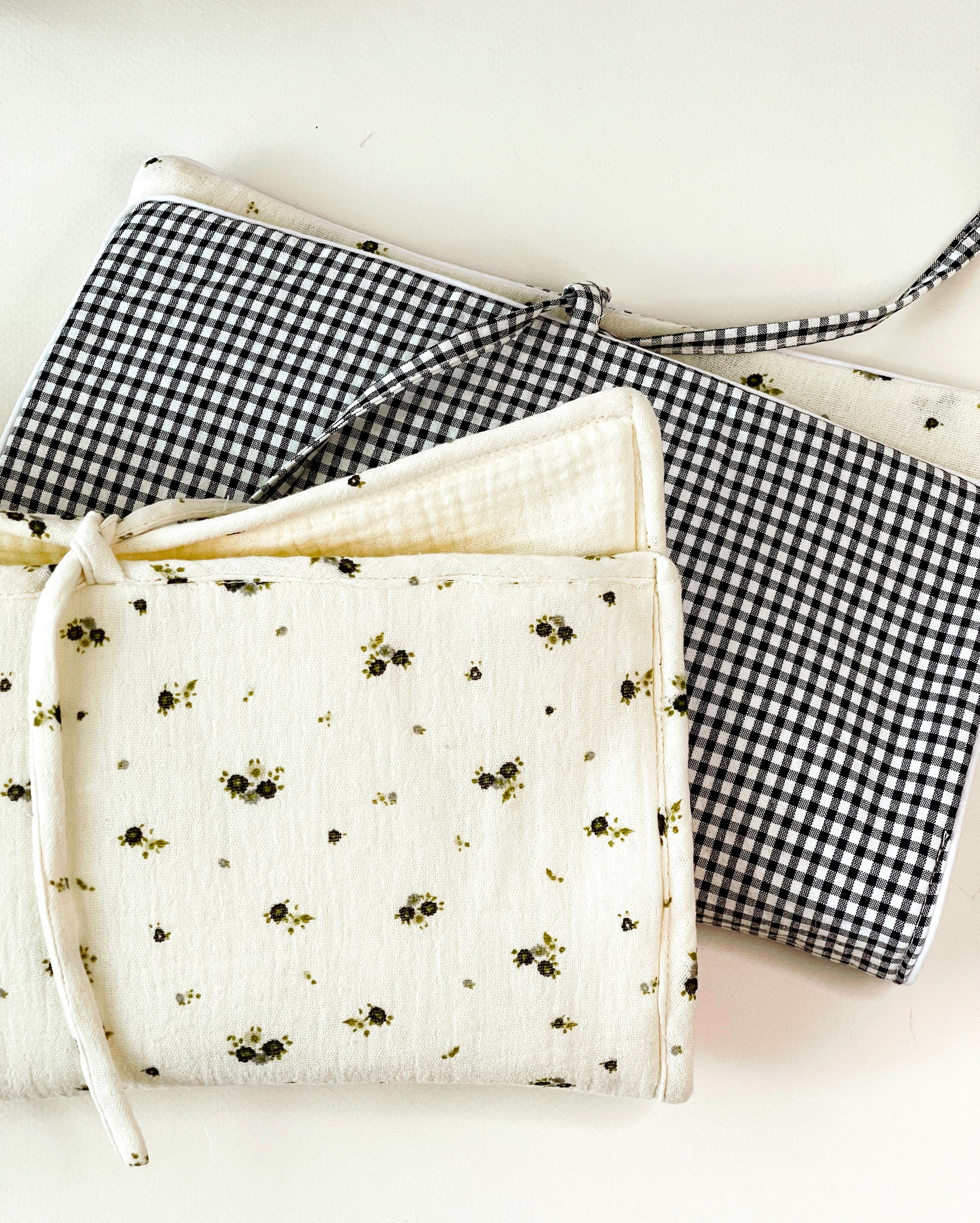 conjunto de  porta toallitas en muselina de flores gris y verde y porta toallitas en estampado de cuadros negros y blancos en el exterior y muselina beis con florecitas en el interior creando una preciosa combinación, ambos con cierre en lazo