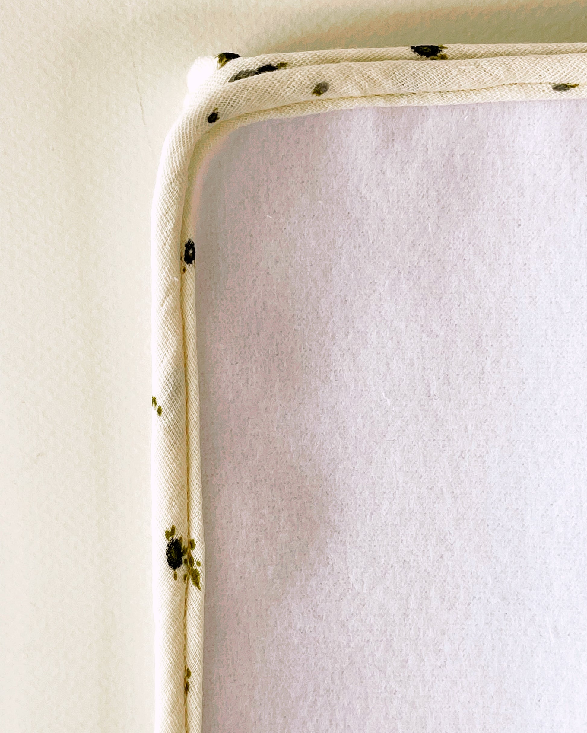 Parte delantera de la alfombra para cambiar al bebé de suave guata. Acabado en cordón de vibo de muselina beis con flores de color gris y verde.