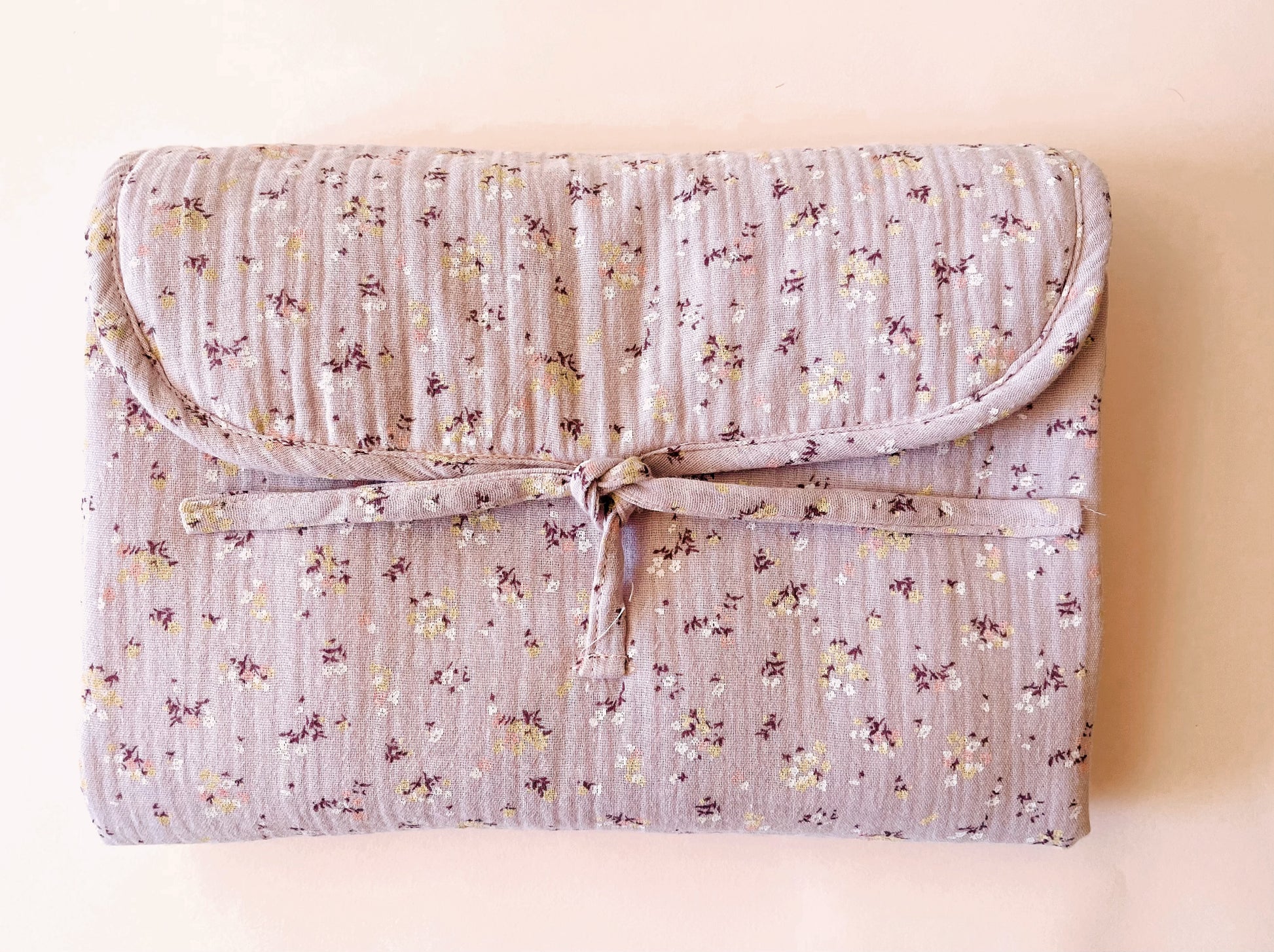 Vista frontal del cambiador de paseo en muselina de color malva con flores amarillas y blancas; cierre con lazo