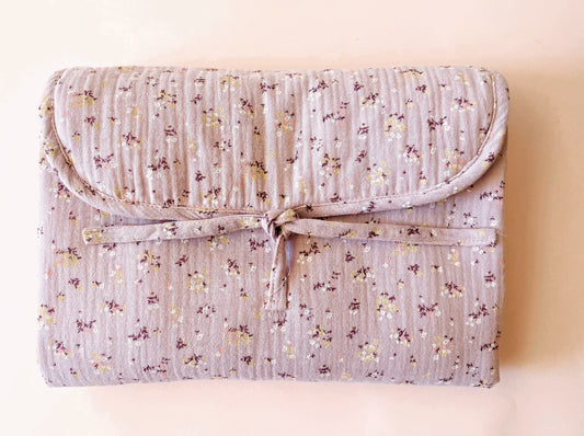 Vista frontal del cambiador de paseo en muselina de color malva con flores amarillas y blancas; cierre con lazo