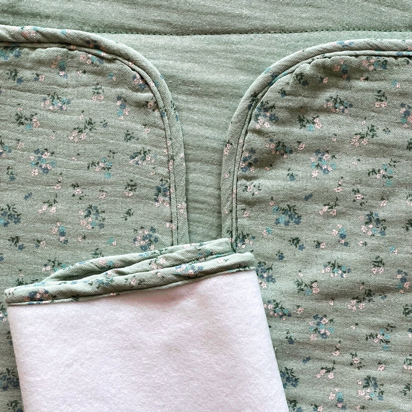 Cambiador de paseo abierto ; la parte interior es de muselina en color verde liso y la parte exterior es de muselina en color verde con florecitas azules y blancas.