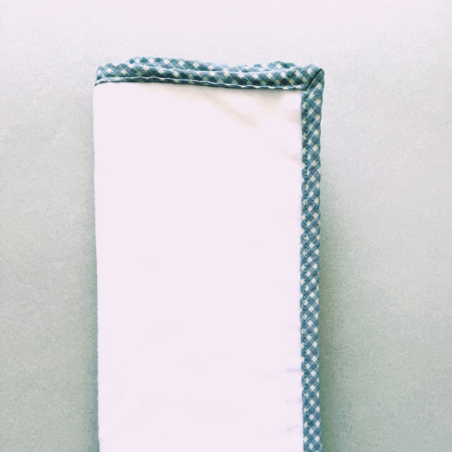 Alfombra que acompaña al cambiador; la parte delantera está confeccionada en una suave guata y la trasera, donde se coloca al bebé, es impermeable . Tiene un bonito acabado de tela de algodón de cuadros de color verde y blanco, de la misma tela que el cambiador.