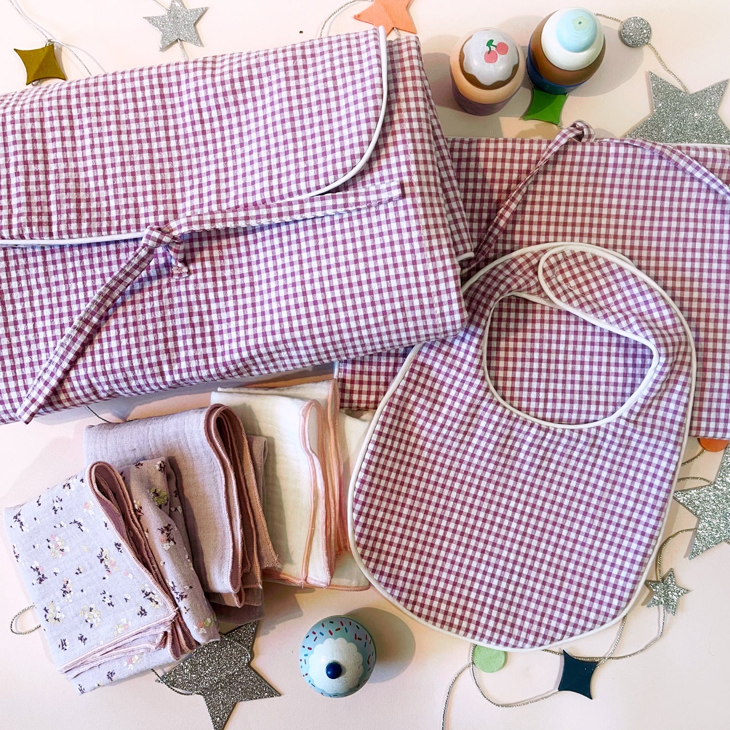 Conjunto de cambiador de paseo en estampado de cuadros rosa claro y blanco junto con el babero y el porta toallitas de estampado cuadros rosa y blanco ; juego de tres muselinas en color malva con flores, malva liso y color blanco liso con acabados en hilo rosa