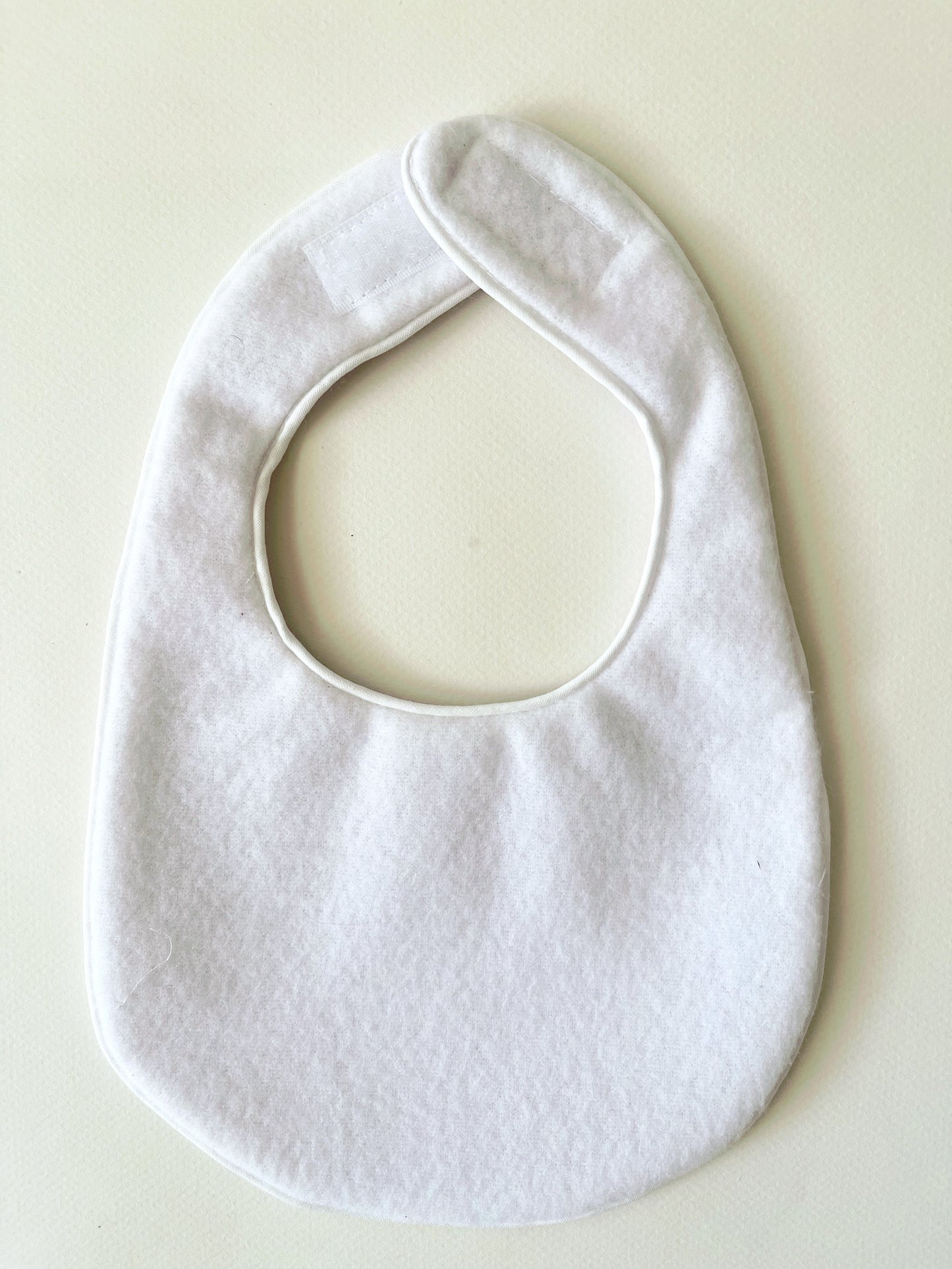 Parte trasera del babero de suave y delicada guata impermeable al tacto, cierre con velcro adaptable al crecimiento del bebe y con un acabado en cordón de vibo de color blanco