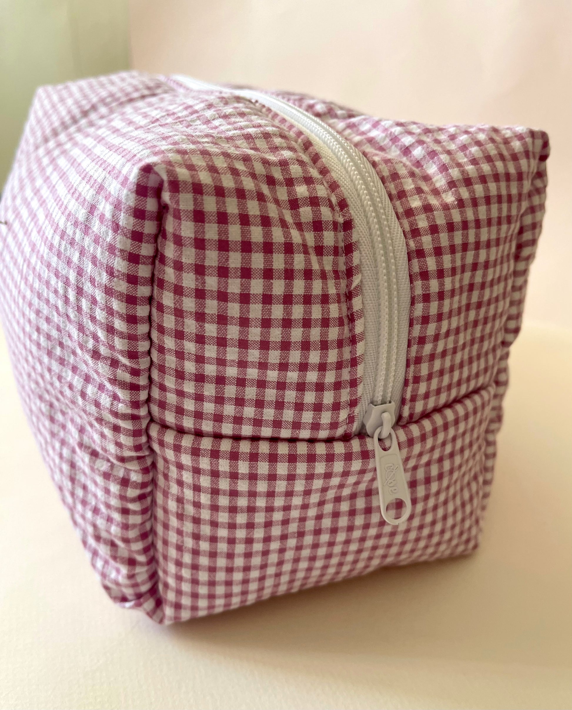 Lateral al detalle del neceser de estampado de cuadros en color rosa claro y blanco con cierre en cremallera