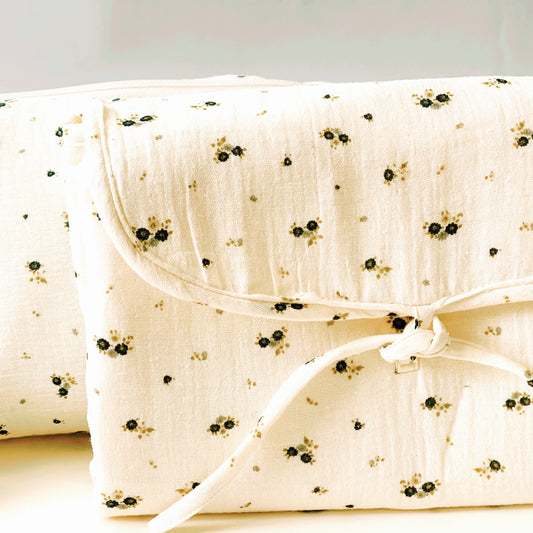 vista frontal del cambiador de paseo de muselina de color beis con florecitas gris y verde ; acabado en cordón de la misma tela y cierre con dos lazos.