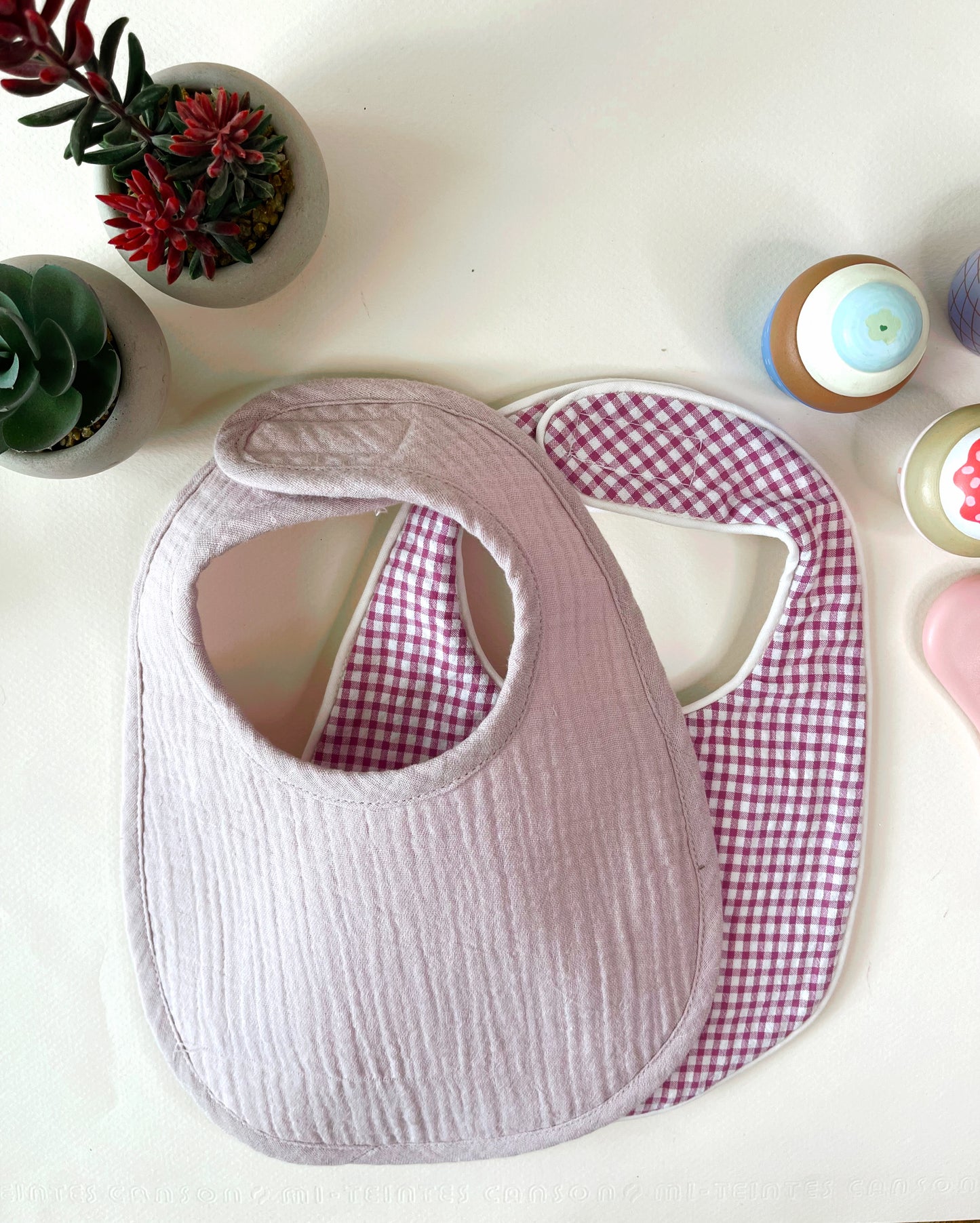 Conjunto de dos baberos de muselina, el de la izquierda en color malva liso y el de la derecha en estampado de cuadros rosa y blanco