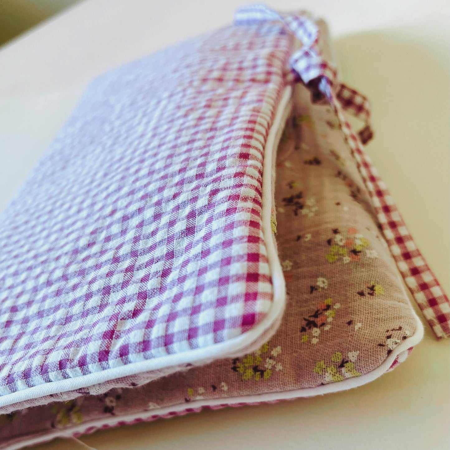 Porta toallitas en tejido de cuadros rosa y blanco en la parte exterior y de muselina malva con flores amarillas y burdeos en la parte interior; cierre con lazo
