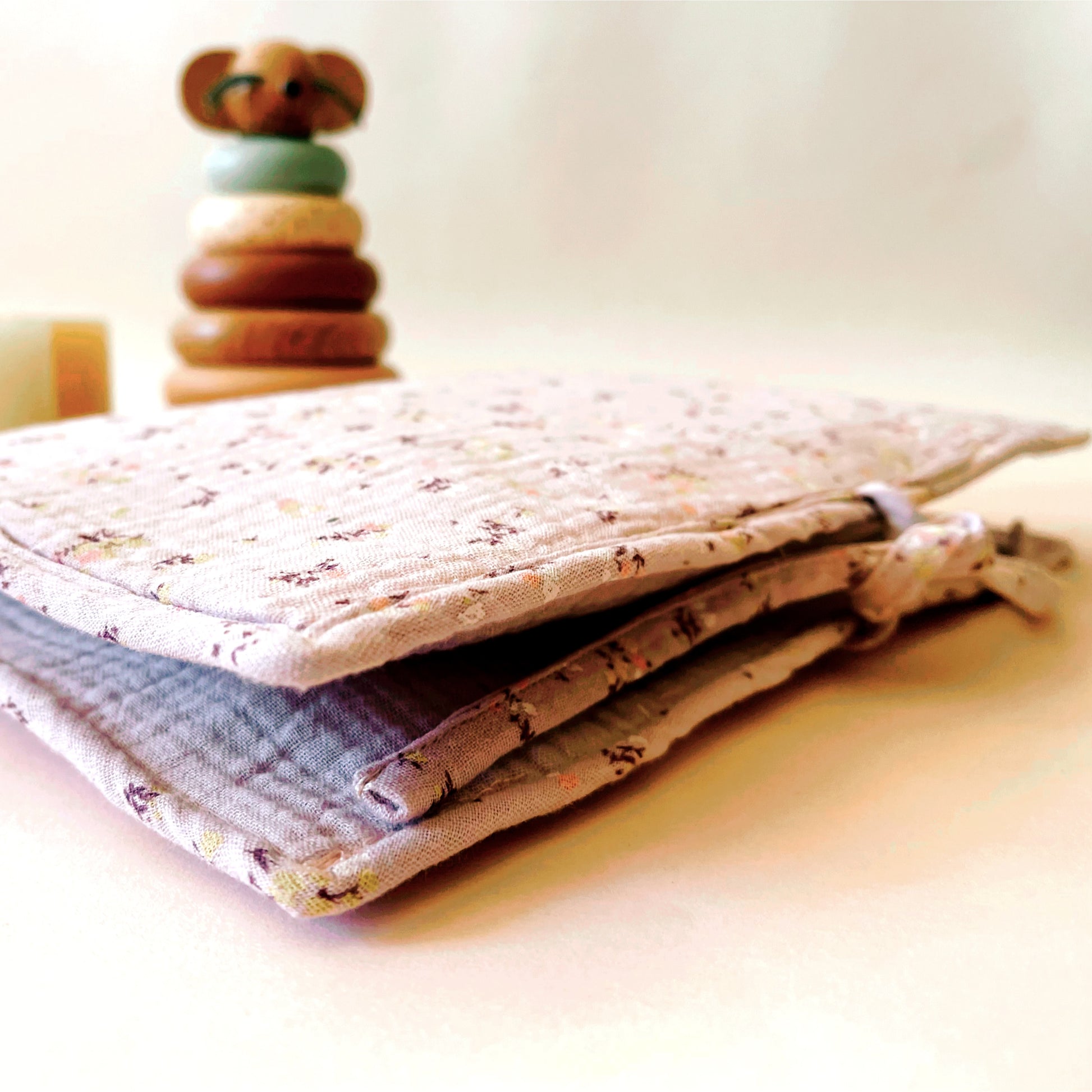 Porta toallitas cerrado con la parte exterior de muselina de color malva con flores amarillas y burdeos y el interior de muselina de color malva lisa. Cierre con dos lazos