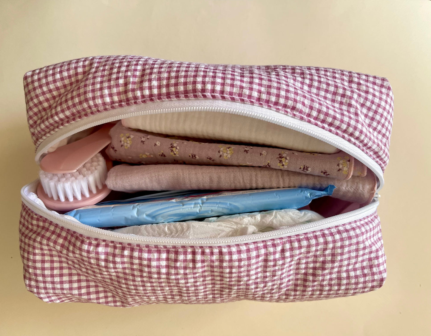 Neceser abierto con amplia capacidad en su interior; dos muselinas en color malva con florecitas y malva liso; pañales y peine de bebé