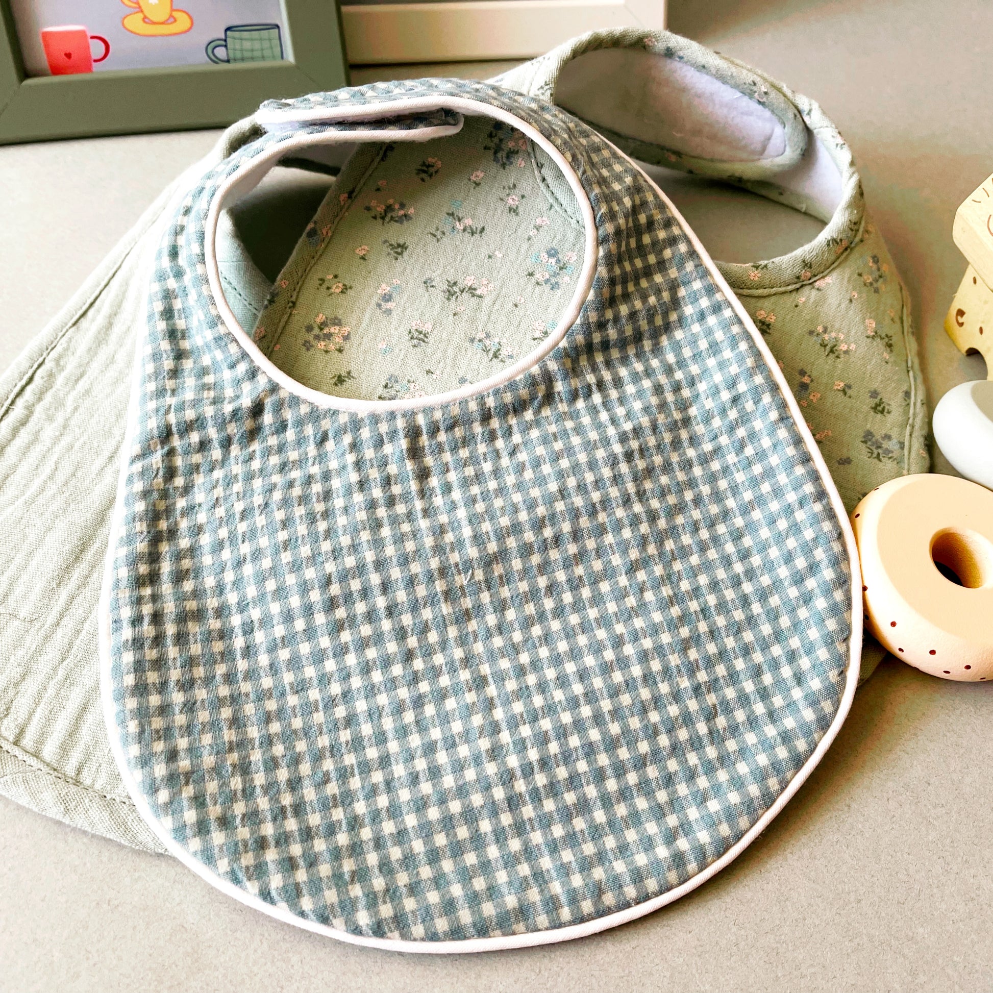 conjunto de babero estampado Vichy de color verde y blanco junto al babero de muselina de color verde con florecitas azules y el de color verde liso. detalle de decoración infantil