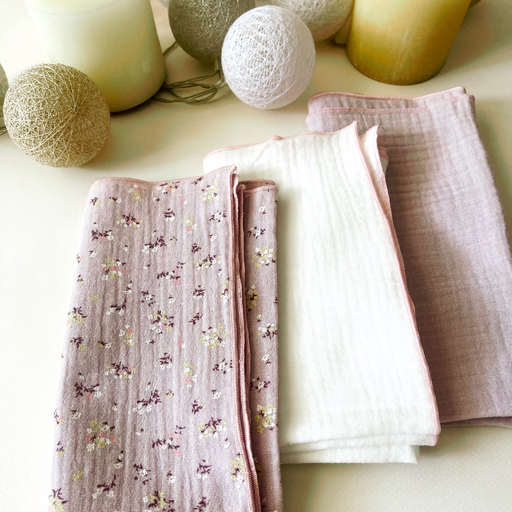 Conjunto de tres muselinas: muselina de color malva con florecitas amarillas y burdeos a la izquierda, en el centro muselina de color blanco y muselina de color malva liso a la izquierda