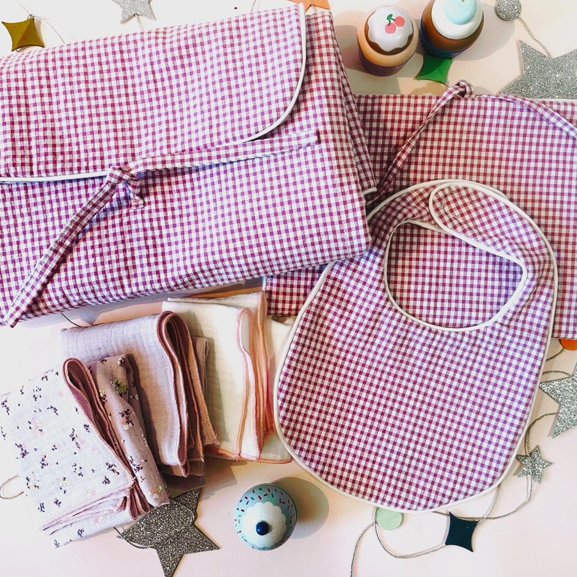 Conjunto de cambiador de paseo en estampado de cuadros rosa claro y blanco junto con el babero y el porta toallitas de estampado cuadros rosa y blanco ; juego de tres muselinas en color malva con flores, malva liso y color blanco liso con acabados en hilo rosa