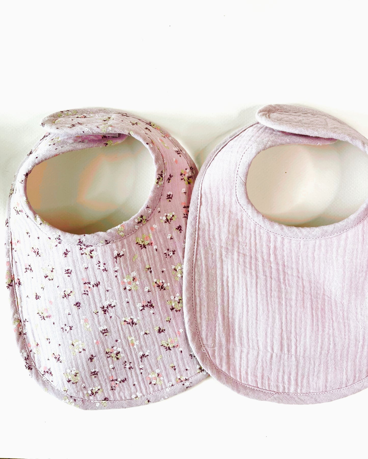 Conjunto de dos baberos de muselina, el de la izquierda en color malva con flores amarillas y burdeos y el de la derecha en color  malva liso