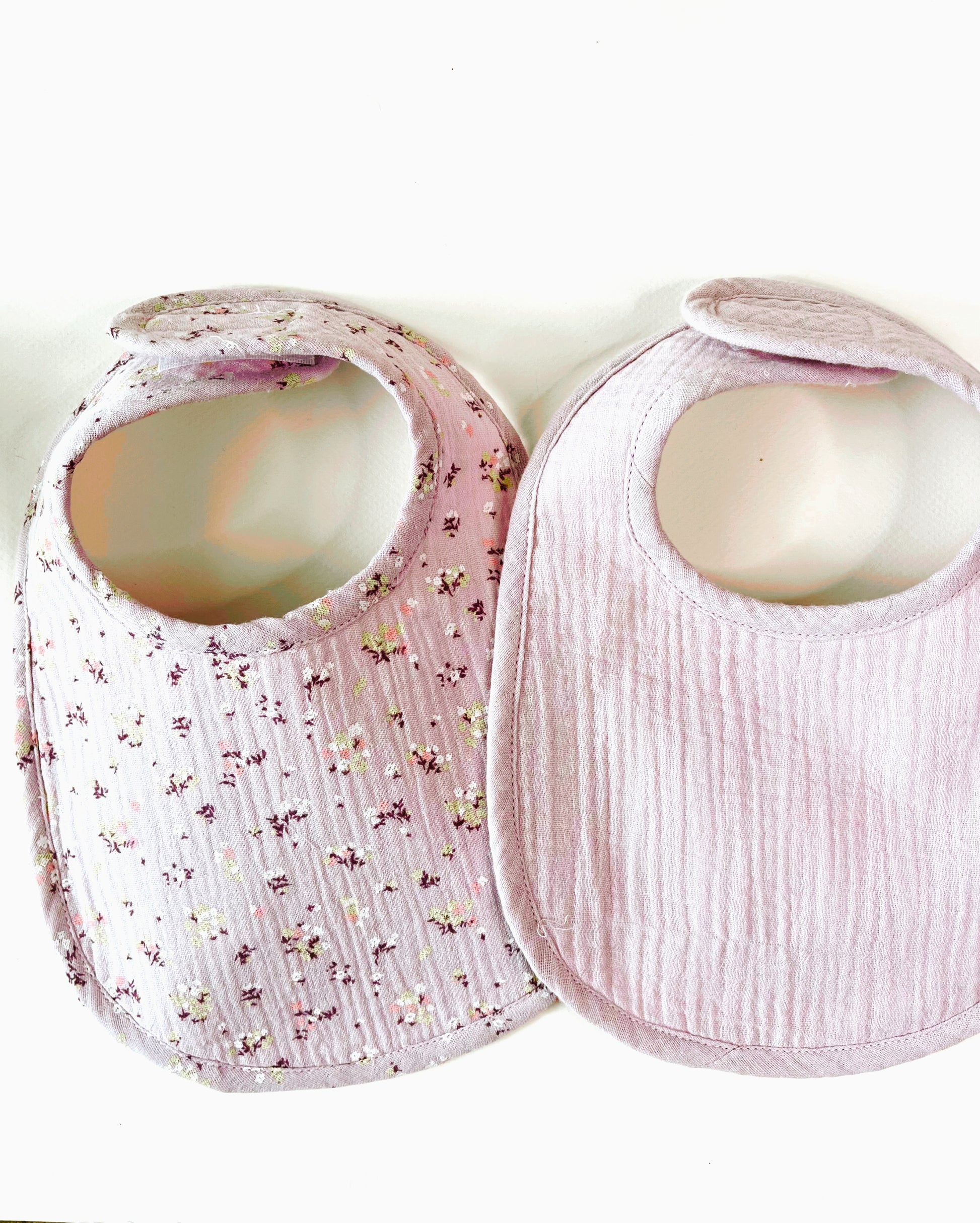 Conjunto de dos baberos de muselina, el de la izquierda en color malva con flores amarillas y burdeos y el de la derecha en color  malva liso