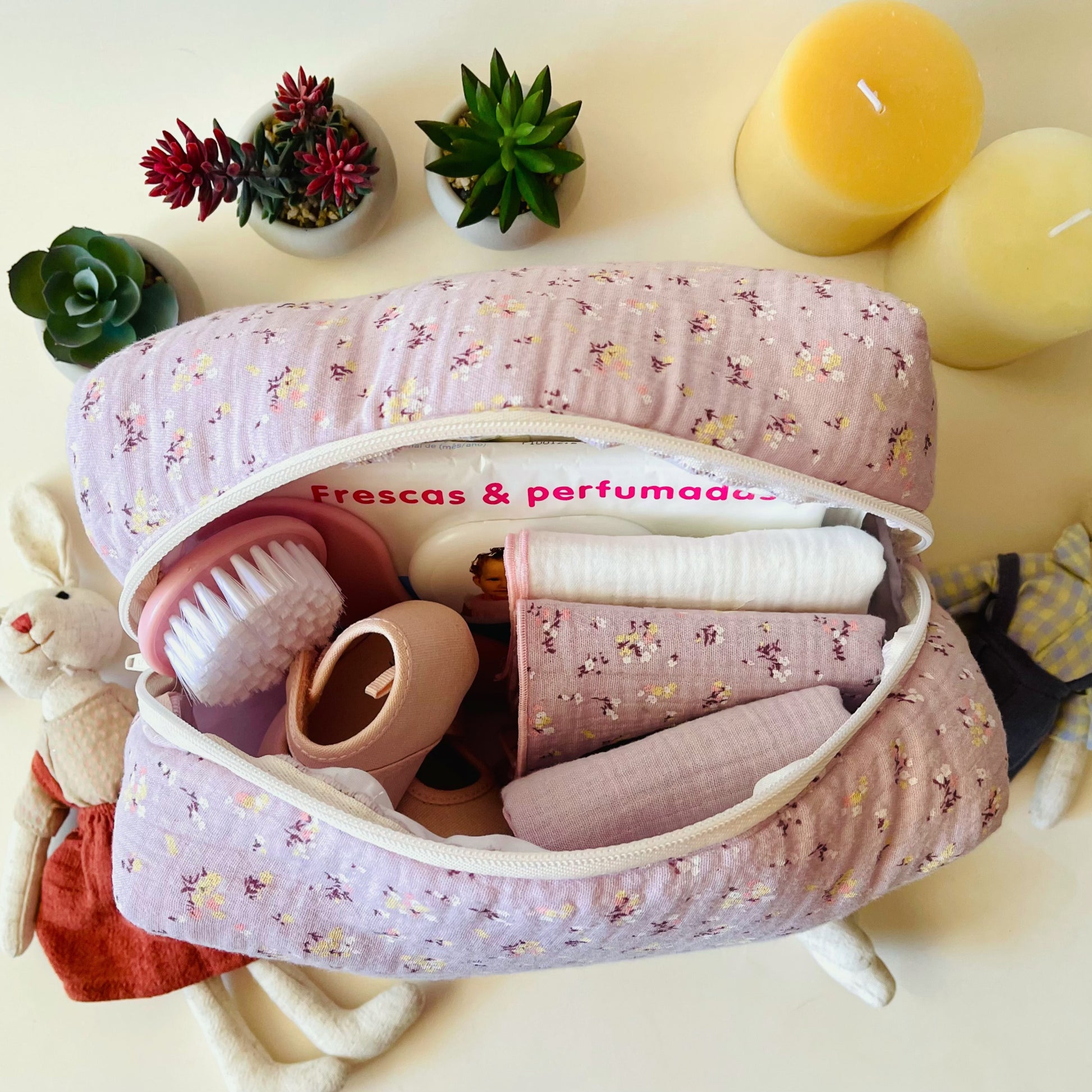 Neceser de muselina de florecitas amarillas y blancas abierto; amplia cremallera de lado a lado del neceser; en su interior conjunto de muselinas de color malva con flores, malva liso y blanco liso.