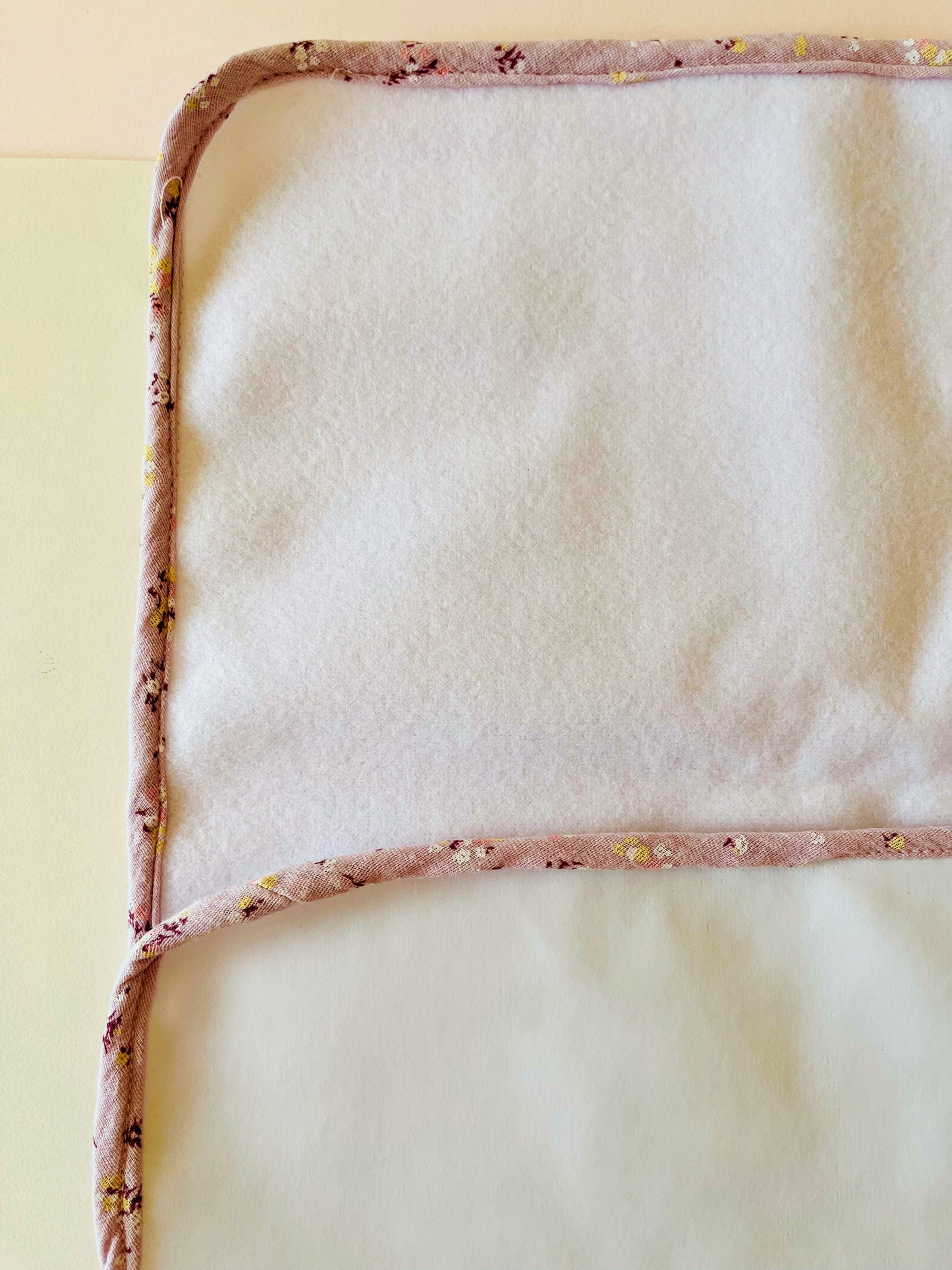 Alfombra del cambiador de paseo de guata impermeable en la parte trasera y en la parte delantera de suave y delicada guata. El borde la alfombra está confeccionada en muselina malva con flores