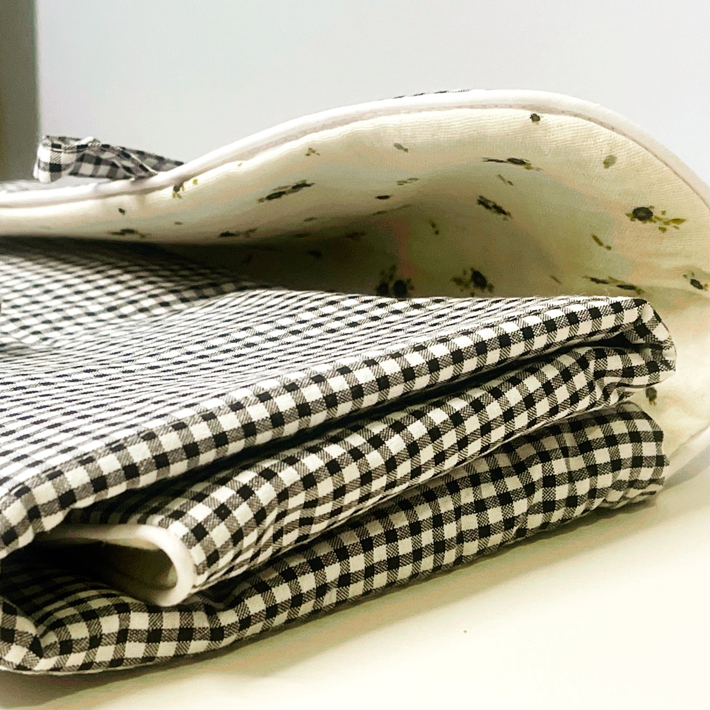 Cambiador de paseo cerrado ; combina el estampado de cuadros negros y blancos en el exterior y en el interior la muselina de color  beis con flores grises y verdes