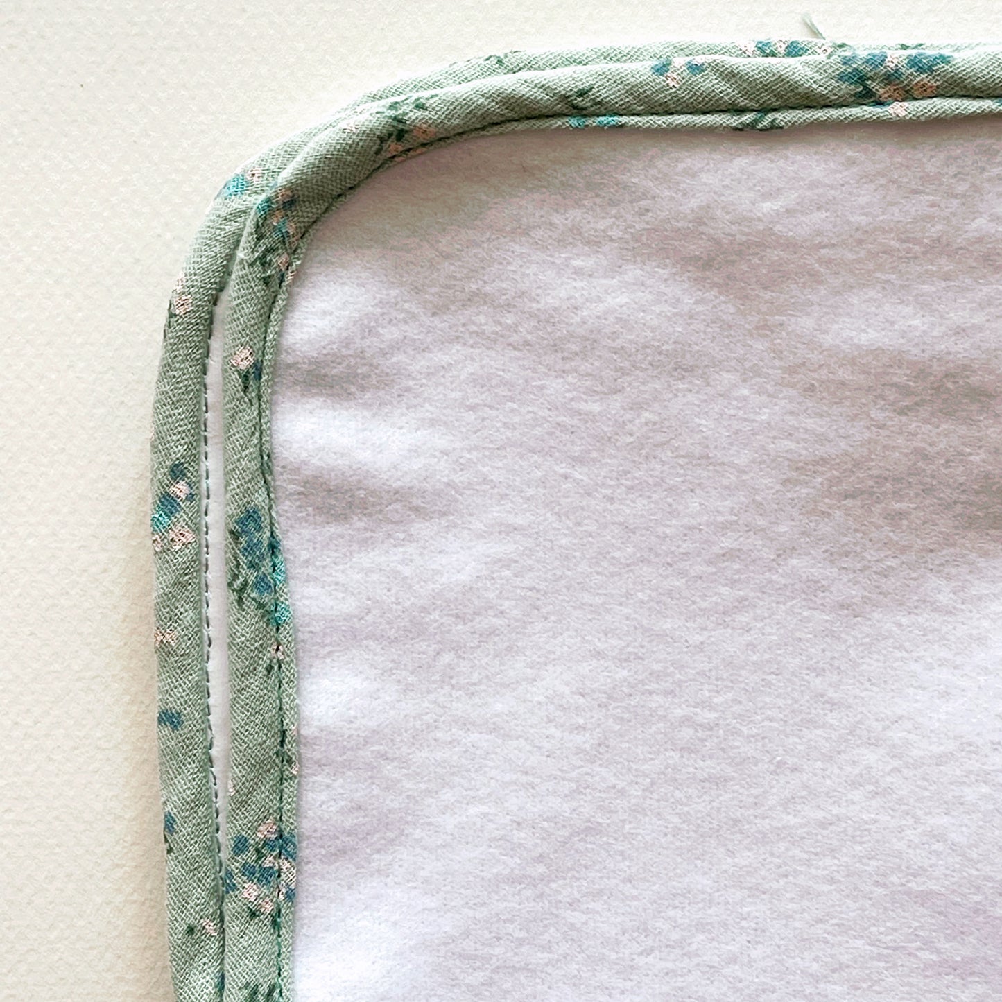 vista de cerca  de la alfombra para cambiar al bebé de color blanco y de suave guata , terminación en tejido de muselina color verde con florecitas