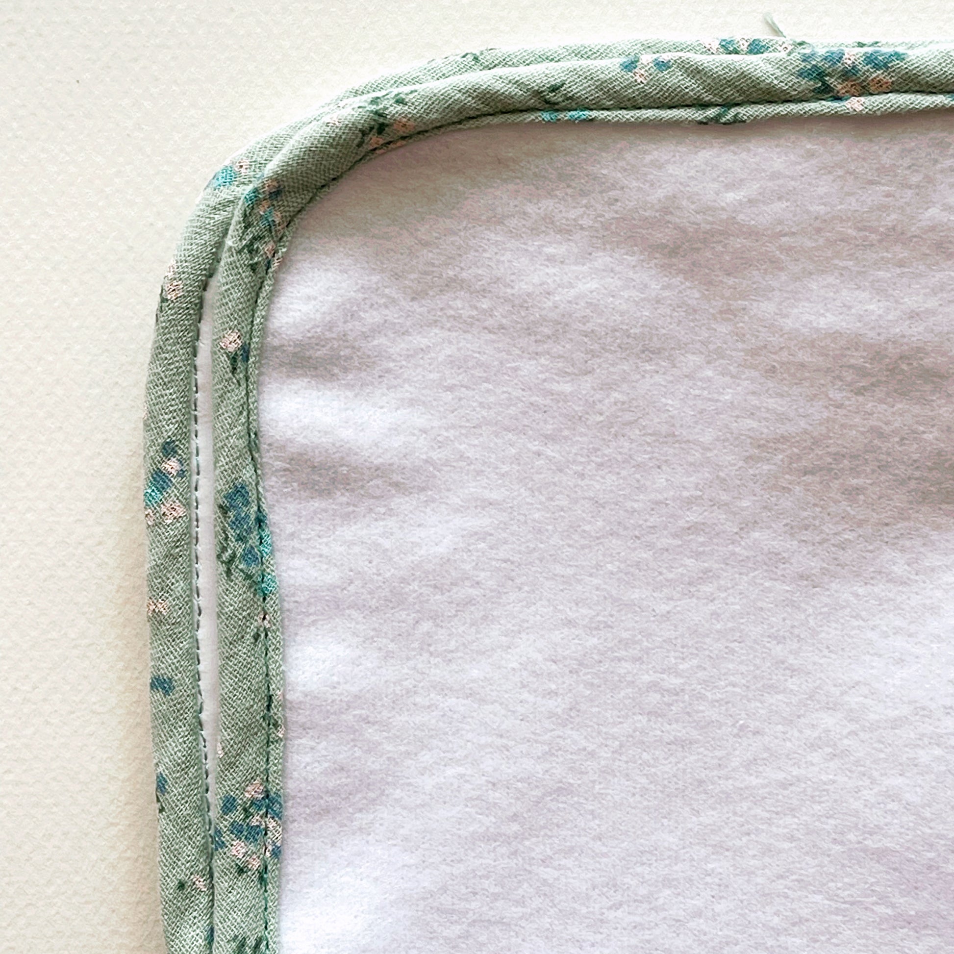 vista de cerca  de la alfombra para cambiar al bebé de color blanco y de suave guata , terminación en tejido de muselina color verde con florecitas