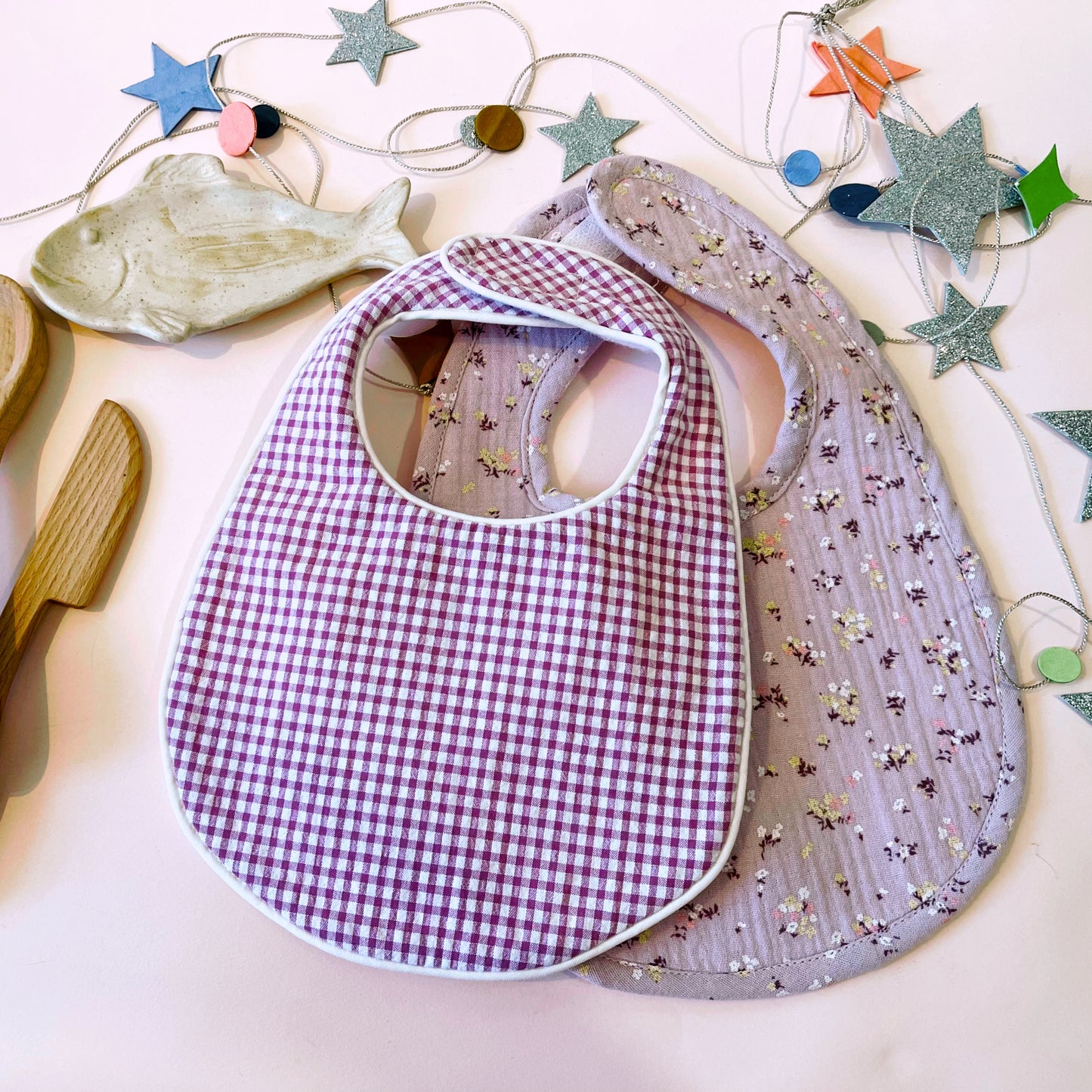 Conjunto de babero de cuadros rosa y blanco junto con babero de muselina de color malva con florecitas amarillas y burdeos; cierre con velcro adaptable al crecimiento del bebé.