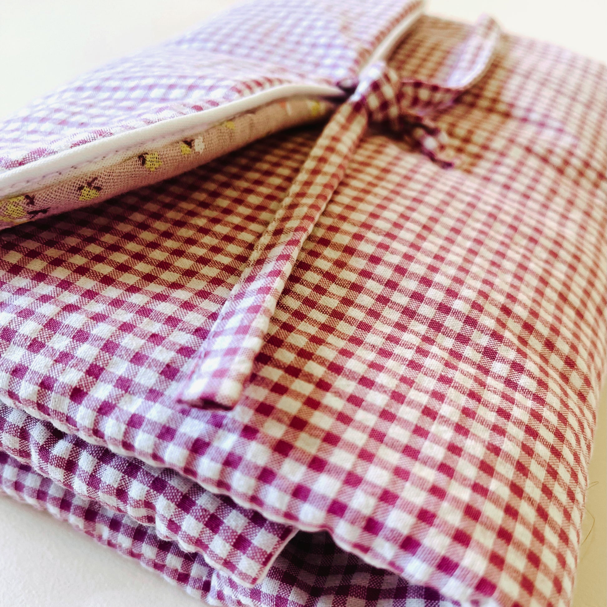 Cambiador de paseo cerrado; en la parte exterior el tejido es estampado de cuadros rosa y blanco y en la parte interior es de muselina de color malva con flores; cierre con dos lazos