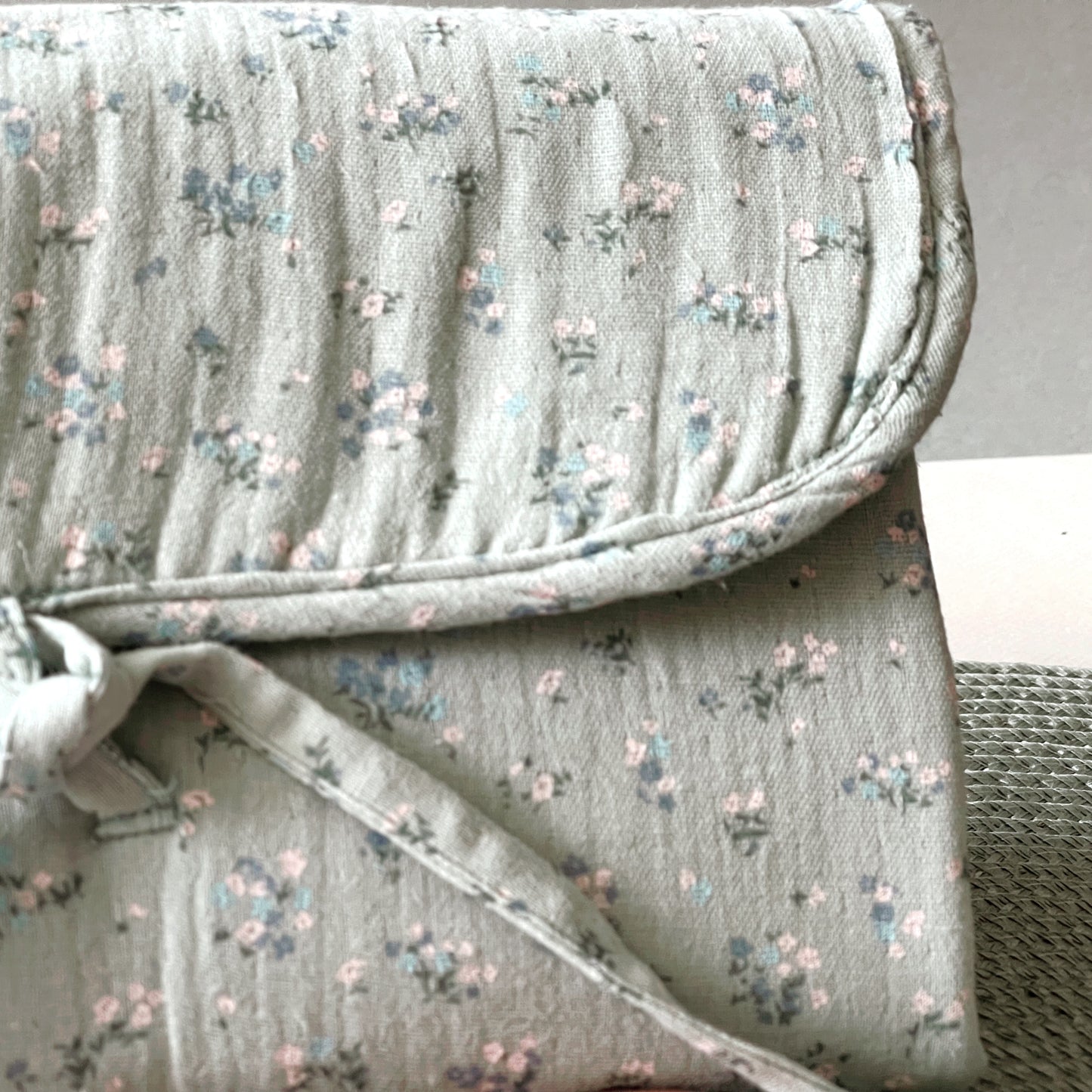 Vista frontal muy de cerca del cambiador de paseo de muselina en color verde menta con flores azules y blancas: cierre con lazo