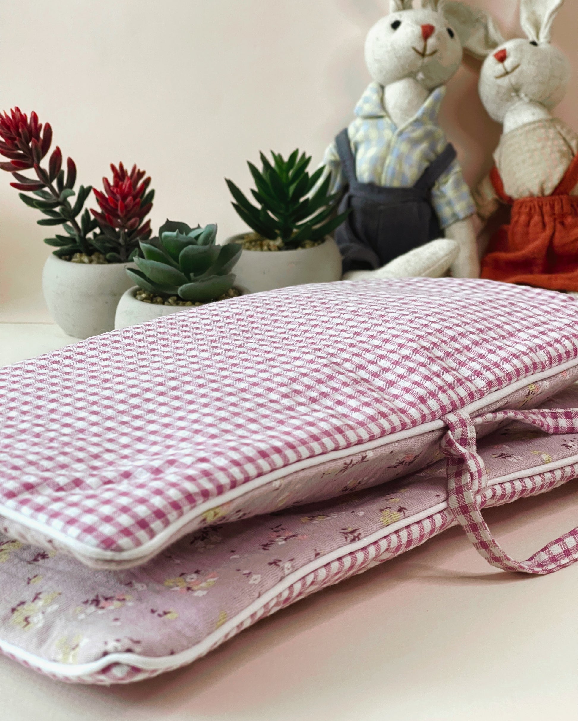 Porta toallitas cerrado y visto de cerca donde se aprecia la combinación de telas; en el exterior la de cuadros en color rosa y blanco y la del interior es de muselina malva con florecitas; cierre con lazo. Decoración dos conejitos de peluche 