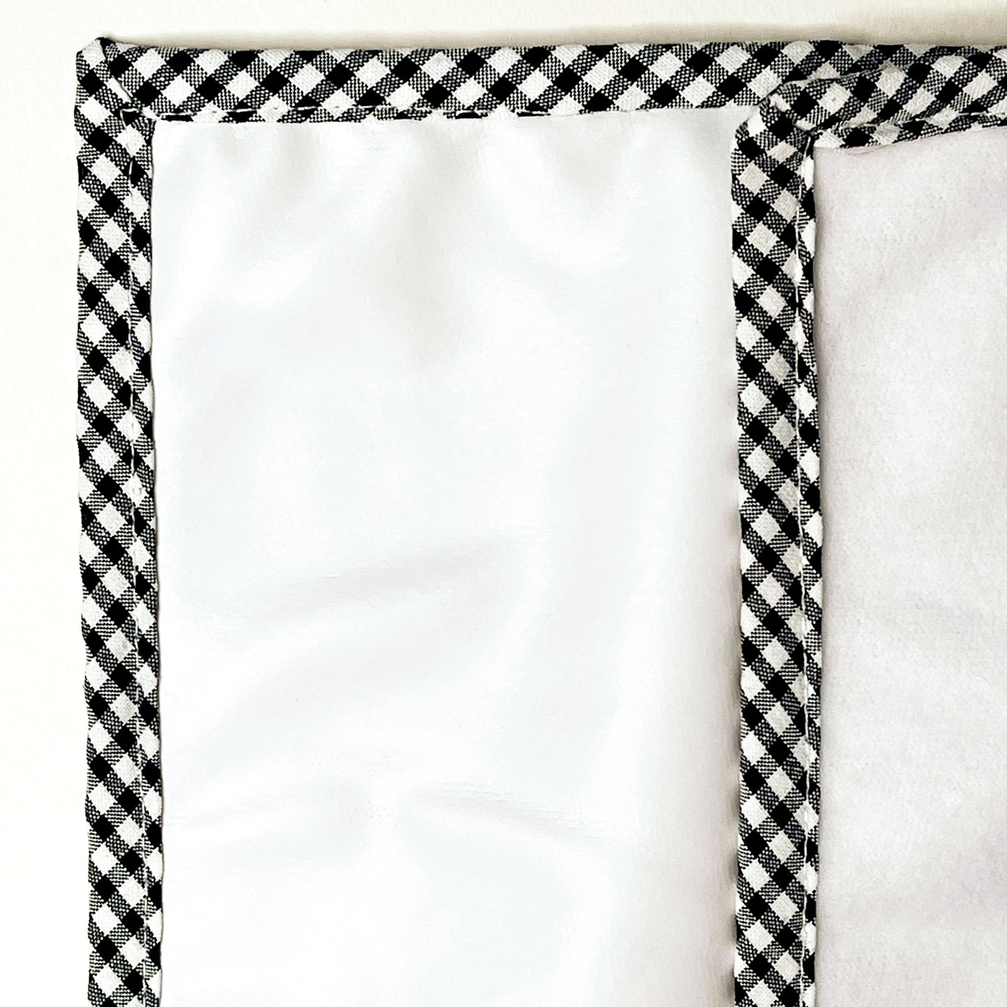 Alfombra del cambiador de paseo para poner el bebé de suave guata en la parte delantera e impermeable en la parte trasera; acabado en estampado de cuadros de color negro y blanco.